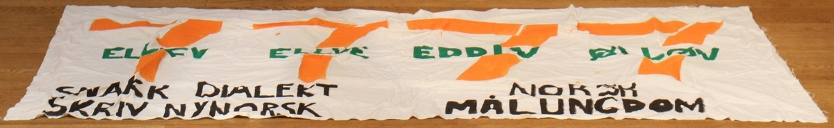 Banner frå arkivet til Norsk Målungdom. På banneret vert logoen til selskapet 7 - eleven omskrive til dialekt. Teksten er: "7 - ellev 7 - ellve 7 - eddiv 7 - ølløv. Snakk dialekt - skriv nynorsk! Norsk Målungdom". Det er truleg at banneret har vore i bruk under ein dialektaksjon for Norsk Målungdom.