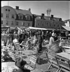 Ett myller av männsikor på Gränna torg. Runt om på torget står marknadsstånd och säljer bland annat kläder och korgar i flätat rotting. Mitt på torget står bord och stolar utställda.