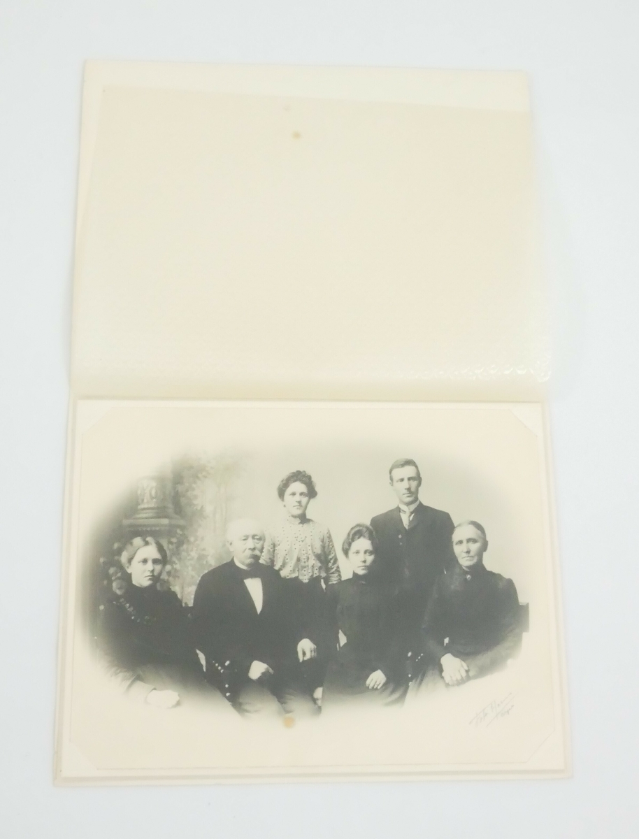 Gruppe med seks mennesker, to menn og fire kvinner. Fire sitter foran på stoler og to står bak. Alle på bildet er voksne med formelle klær, sannsynligvis er det en familie. 