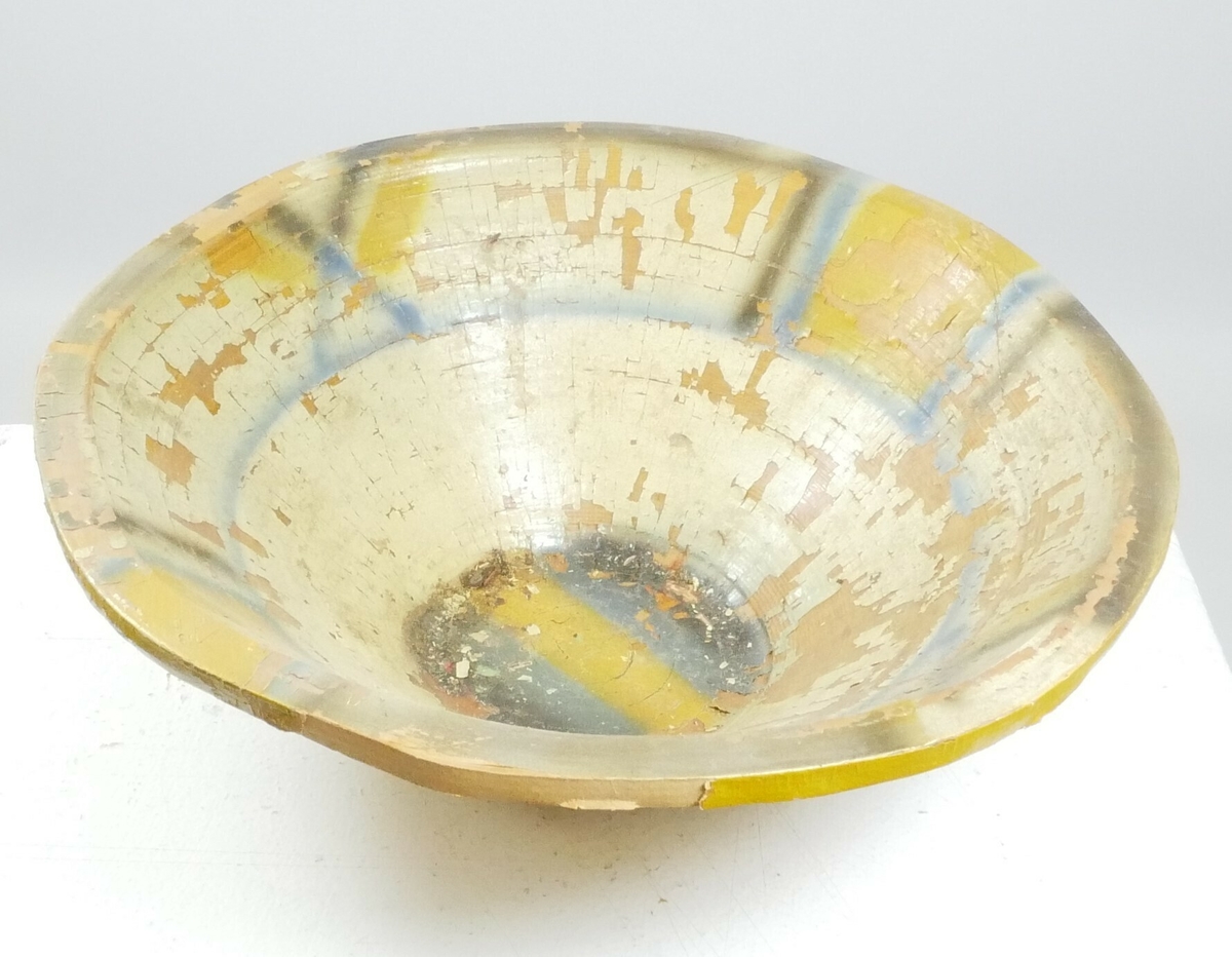 Rund dyp skål i tre som smalner innover. Innsiden er malt i mønster i gult, grønt og blått, utsiden er malt gul. 