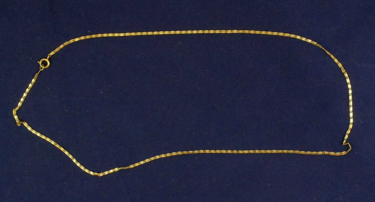 Hvit rektangulær pappemballasje med lokk. Inne i esken er det tre halskjeder. 

Halssmykke med gule steiner. 

Halssmykke to tekstiltråder med hvite steiner, en lås i enden

Gullfarget halssmykke 