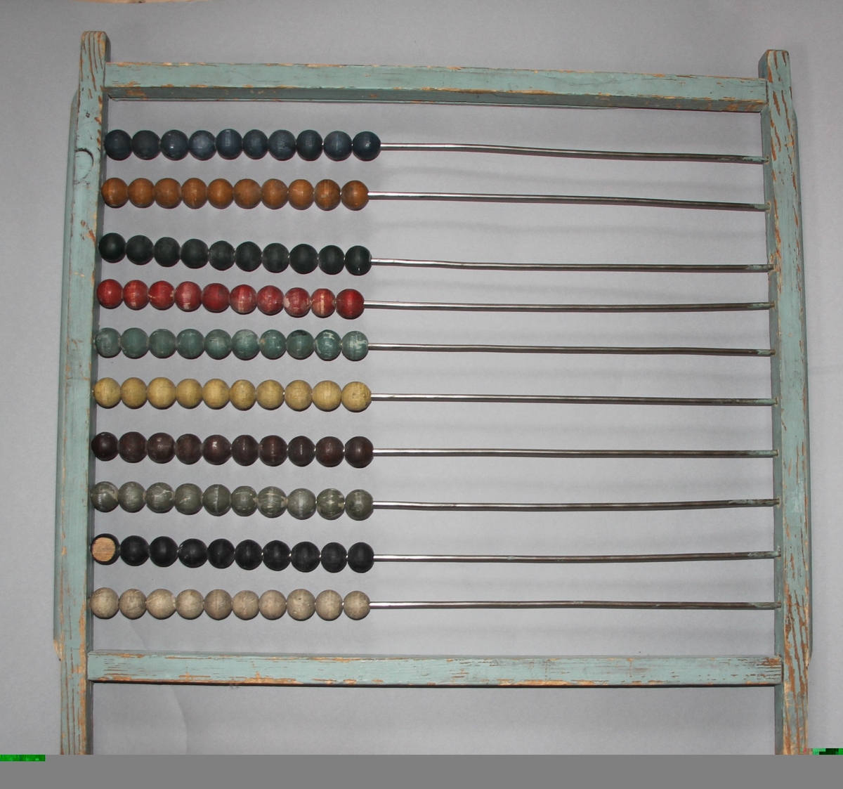 Kuleramme i tre med metallstengar. Trekuler i ulike fargar er tredd på metallstengane.Sjølve ramma er einsfarga, måla i ljos farge.