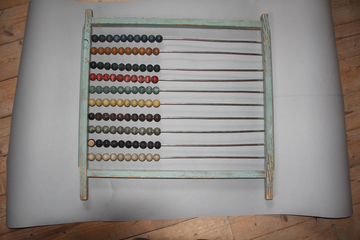 Kuleramme i tre med metallstengar. Trekuler i ulike fargar er tredd på metallstengane.Sjølve ramma er einsfarga, måla i ljos farge.