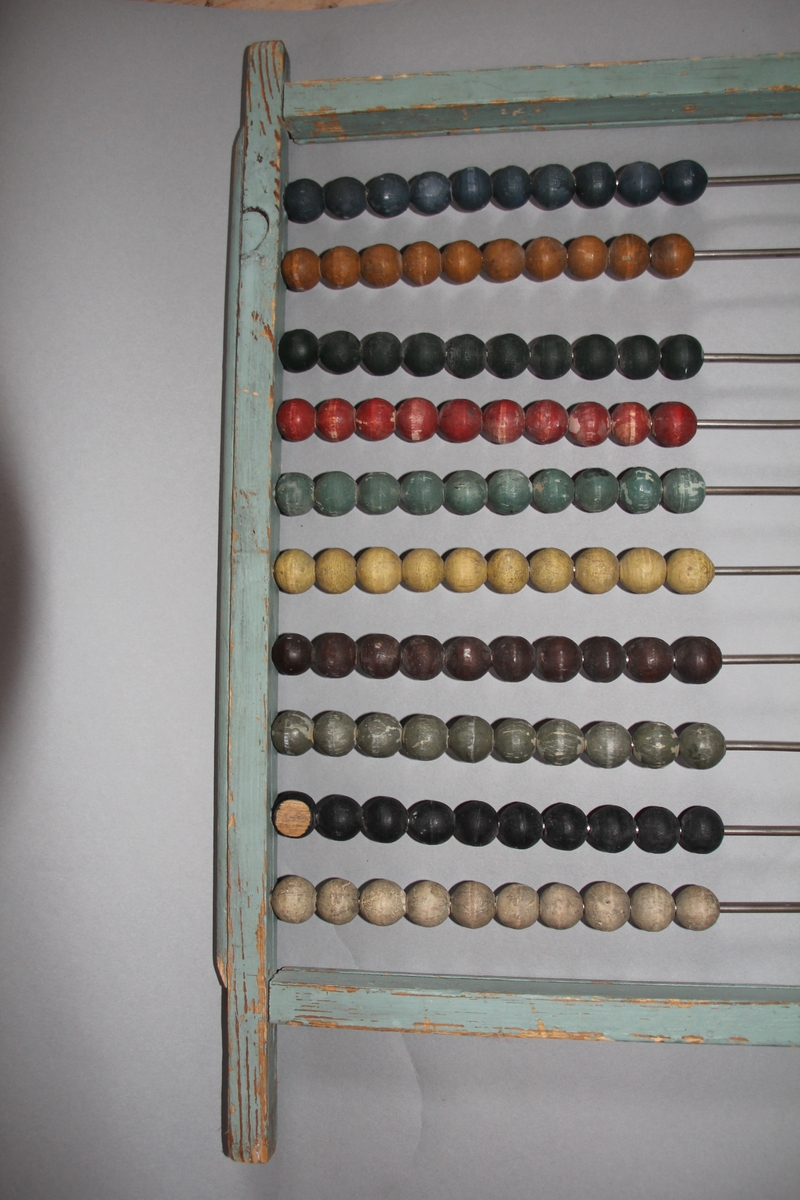 Kuleramme i tre med metallstengar. Trekuler i ulike fargar er tredd på metallstengane.Sjølve ramma er einsfarga, måla i ljos farge.