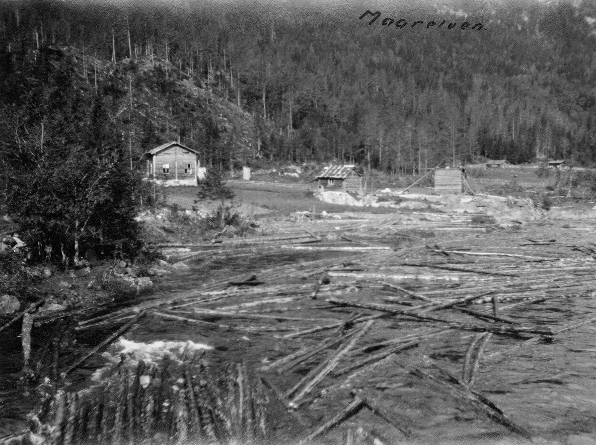 Fløtingstømmer i elva Mår i Tinn kommune i Telemark.  Fotografiet er tatt fra Gausetbrua, der elveløpet var forholdsvis vidt og grunt, og hvor tømmeret stundom kunne sette seg fast på stein- og grusører.  Ved elvebredden ser vi bebyggelsen og innmarka på eiendommen Sandviken, som ligger på den sørvestre sida av vassdraget.  Bakenfor ser vi ei forholdsvis bratt li med barskog.  Mår kommer fra Mårvatn og den regulerte Kalhovdfjorden.  Vassdraget er om lag 35 kilometer langt, og det ble fløtet tømmer fra Raunehølen, 22-23 kilometer fra utløpet i nordenden av Tinnsjøen.  På denne strekningen har elva et fall på 624 meter, inkludert en del stryk og fossefall, som gjorde det vanskelig å fløte lange stokker her.  Arbeidet og fløtingskostnadene ble fordelt på fire roter.  Gausetbrua, der dette fotografiet er tatt ligger like nedenfor Bråbrekkfossen og Bråbrekkhølen, som var delet mellom andre og tredje rote.  Dette fotografiet skal være tatt like etter at fløterne hadde rensket den ovenforliggende Bråbrekkhølen for tømmer.  Fløtinga i Mår pågikk som regel i 12-14 dager, og vanligvis fikk man tømmeret ned til Tinnsjøen i løpet av en sesong.