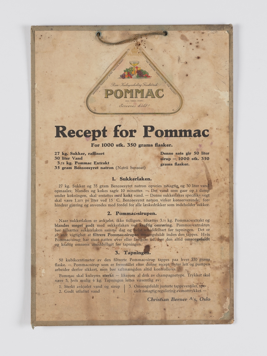 skrift, pålimt etikett til varen "Pommac", med stilleben av frukt og et stettglass