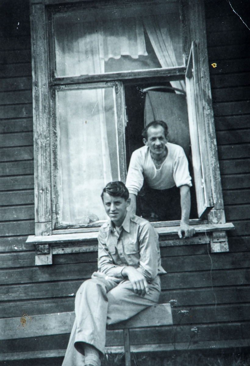 2 menn, Kåre Bakken sittende foran et åpent vindu. Mannen stående bak, er ukjent.