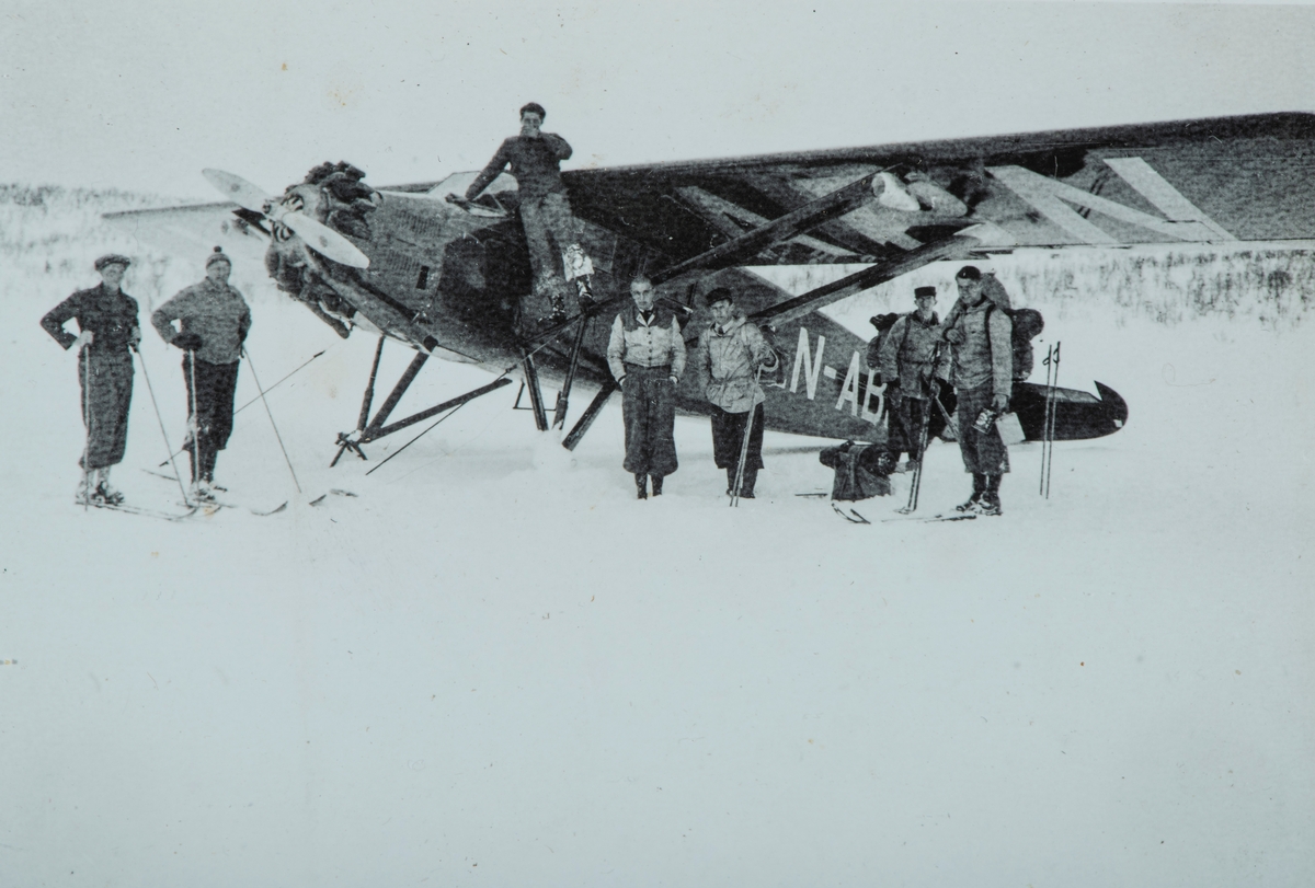 Gruppe 7 ukjente, 1 fly på bakken. Snø,Vinter. Stinson SM-1, LN-ABN fra Norsk Lufttrafikk.
1 mann sittende på flyet, resterende står med ski og sekker.
Bilde er hentet fra et album med primært bilder fra Stange området.