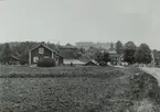 Greksåsars hytta. Foto från väster. Framför hyttan är råstutaket, vid sidan maskinhuset med lokomobilen. Husen till vänster tillhör gästgivaregården. Längst till höger handelsboden, på före detta posthemmanets plats. Mellan maskinhuset och handelsboden syns norra längan i Sexmansgården, d.v.s. den bodlänga som flyttades till Skansen i Stockholm.
Fotot tagen efter år 1895.