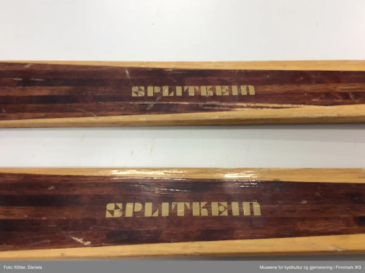 Tofarget treski med Kandaharbindinger. Bak bindingen er det påført deler i rød kunststoff for bedre feste med skoen. Helt bak har skiene en metallkant.
