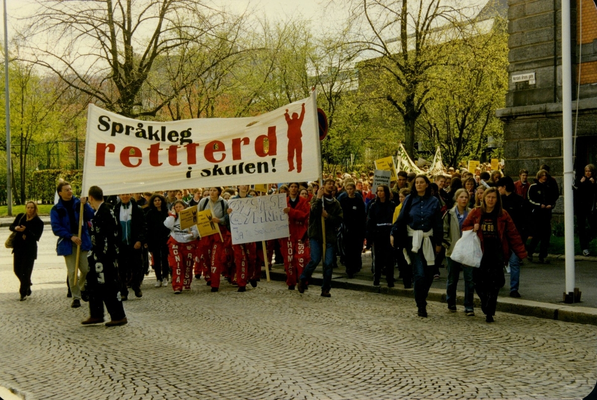 Fotografi frå arkivet til Norsk Målungdom. Biletet er teke i Bergen under Aksjon for språkleg rettferd i skulen (AFSRIS) i 1997. AFSRIS var eit samarbeid mellom Norsk Målungdom, Norsk Elevorganisasjon og Norsk Gymnasiastsamband, som arbeidde mot å fjerne retten til læremiddel på nynorsk. Det er uvisst kven fotografen er.

Dette er eit av fleire foto frå arkivet til Norsk Målungdom. For innsyn ta kontakt med Nynorsk kultursentrum.