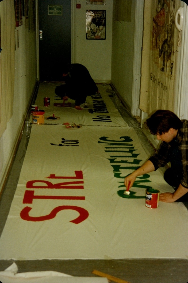 Fotografi frå arkivet til Norsk Målungdom. Biletet viser måling av banner til Aksjon for språkleg rettferd i skulen (AFSRIS) i Bergen i 1997. AFSRIS var eit samarbeid mellom Norsk Målungdom, Norsk Elevorganisasjon og Norsk Gymnasiastsamband, som arbeidde mot å fjerne retten til læremiddel på nynorsk. Det er uvisst kven fotografen er.

Dette er eit av fleire foto frå arkivet til Norsk Målungdom. For innsyn ta kontakt med Nynorsk kultursentrum.