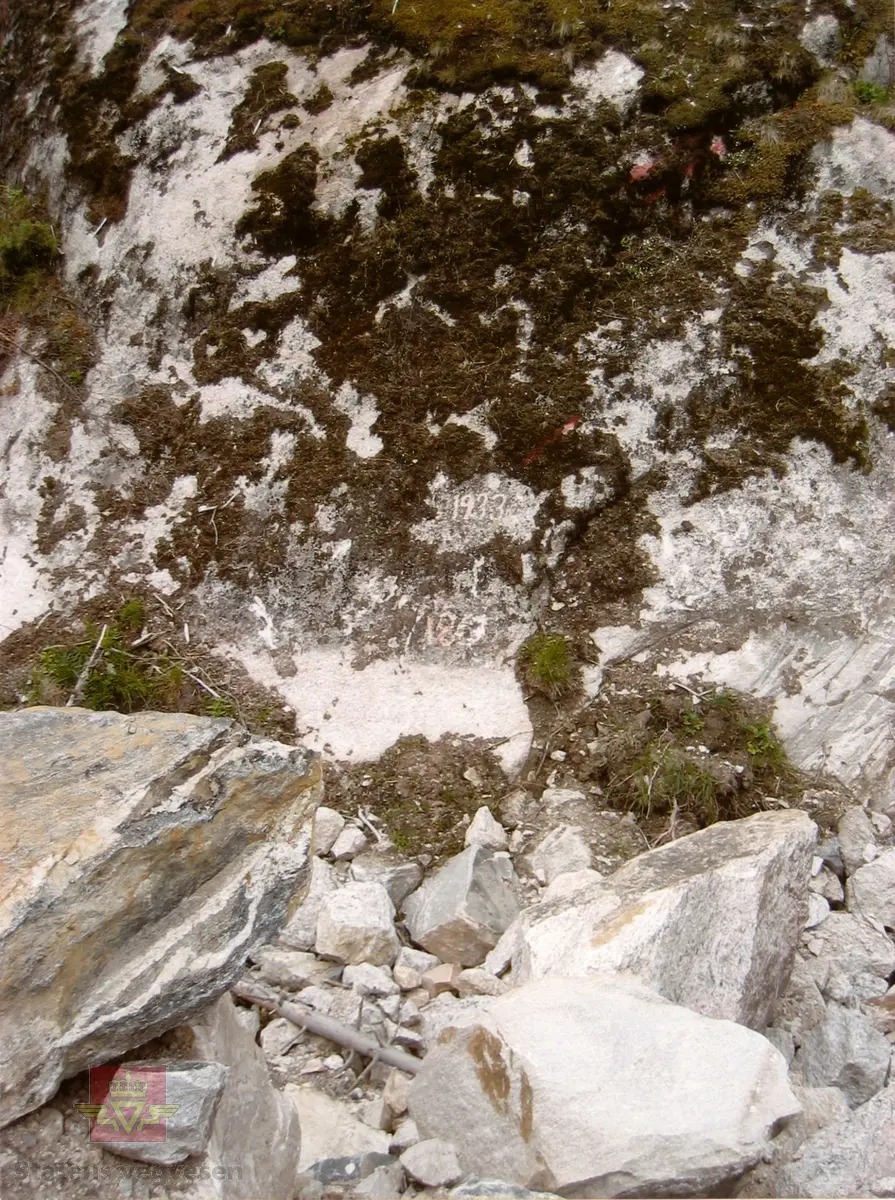 Flommerke hogd i fjell med årstallene 1897 og 1933. Ligger bak nyere rasvoll i nordenden av vannet. Riksvei 9 hovedparsell 7 km 6,319. 
For oversikt, se bilde NVM 09-F-00407.

Ikke registrert i prosjektet utført av Næs Jernverksmuseum på oppdrag for Statens vegvesen  i 2012.

Stedsnavn: Flåne