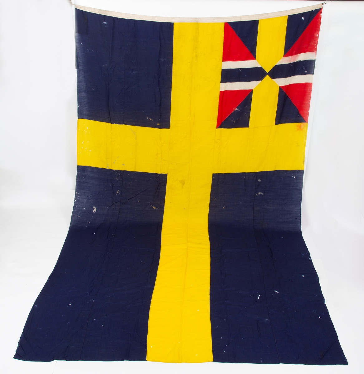 Svensk flagg med unionsmerke, "sildesalaten". Metallhempe. Møllspist og slitt.
Unionsmerket: 120 x 103

Givers datter opplyser at flagget var kjøpt på auksjon eller loppemarked på 1980 tallet. Det skal ha kommet fra båtbyggeriet på Kugrava i Son.