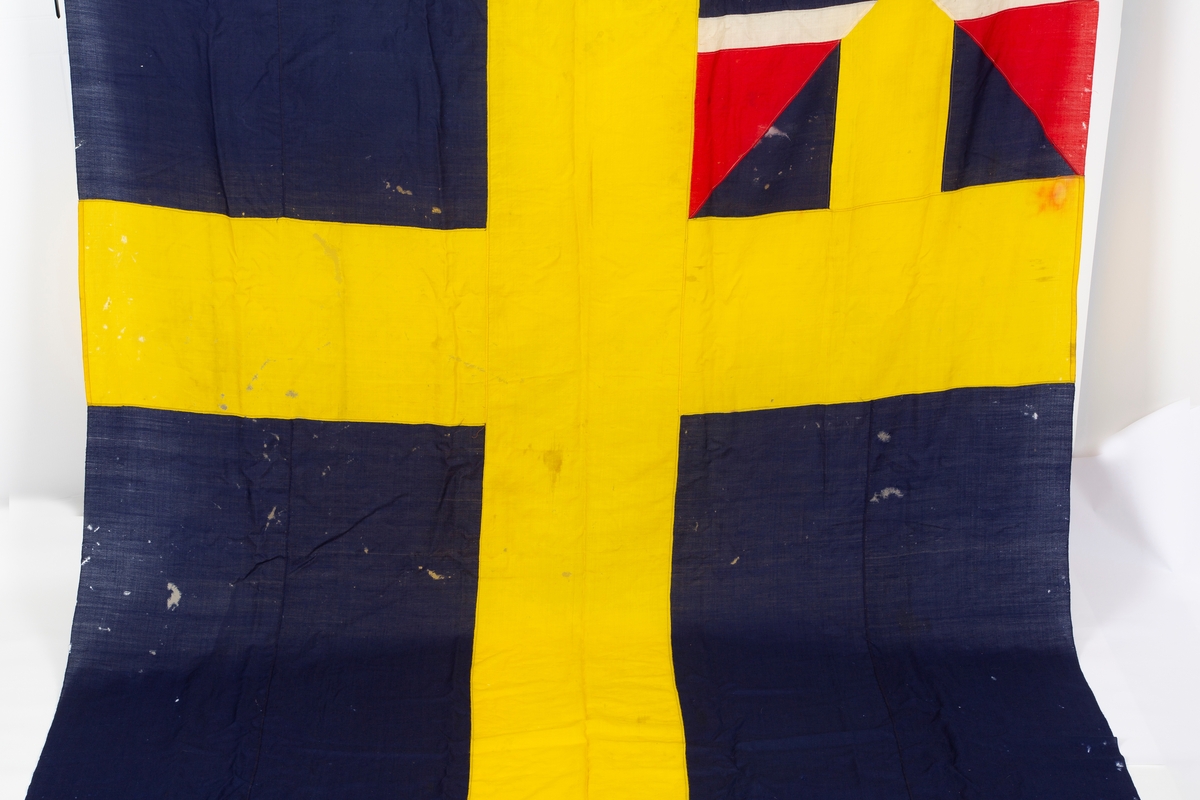 Svensk flagg med unionsmerke, "sildesalaten". Metallhempe. Møllspist og slitt.
Unionsmerket: 120 x 103

Givers datter opplyser at flagget var kjøpt på auksjon eller loppemarked på 1980 tallet. Det skal ha kommet fra båtbyggeriet på Kugrava i Son.