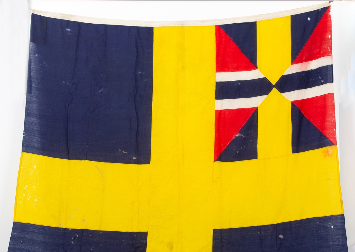 Svensk flagg med unionsmerke, "sildesalaten". Metallhempe. Møllspist og slitt.
Unionsmerket: 120 x 103

Givers datter opplyser at flagget var kjøpt på auksjon eller loppemarked på 1980 tallet. Det skal ha kommet fra båtbyggeriet på Kugrava i Son.