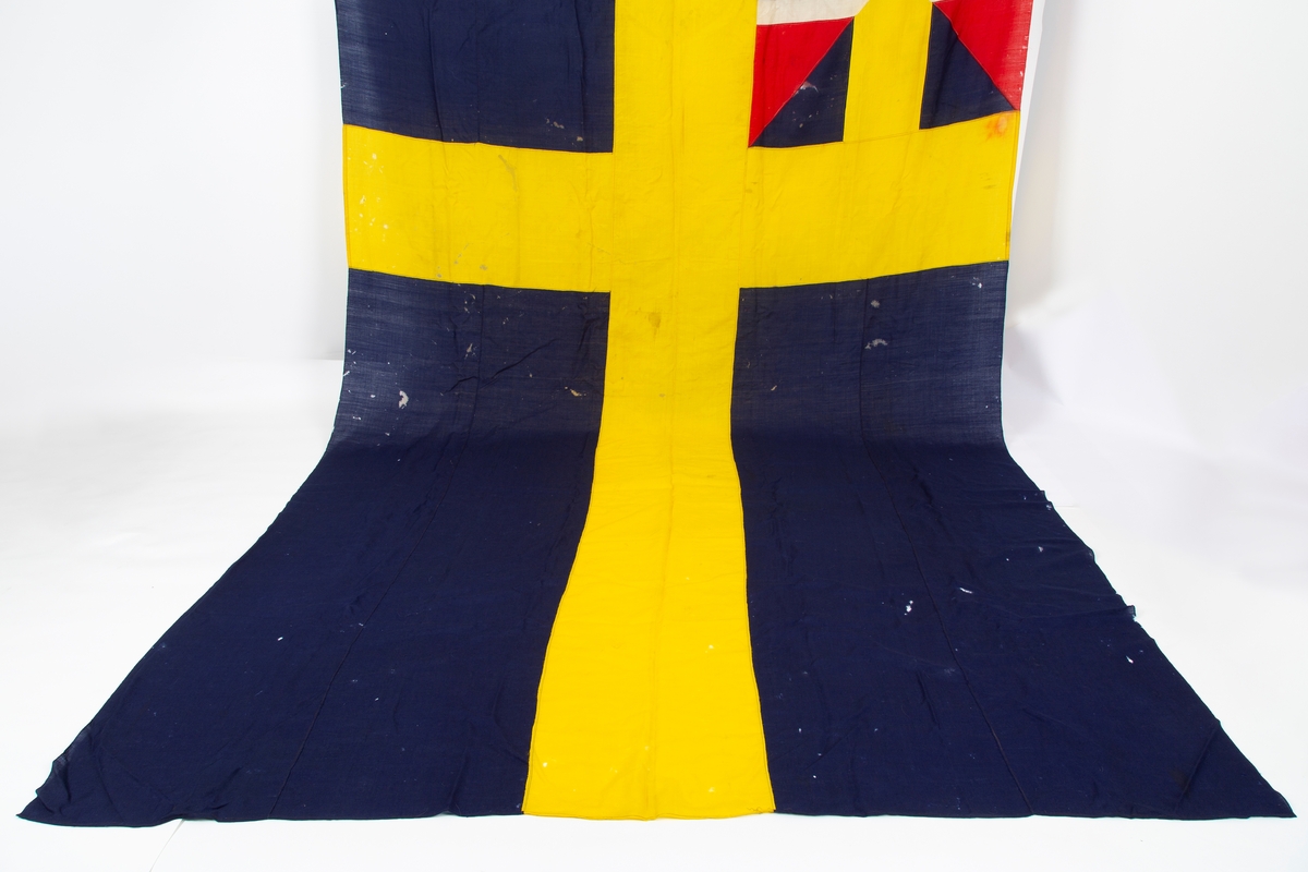 Svensk flagg med unionsmerke, "sildesalaten". Metallhempe. Møllspist og slitt.
Unionsmerket: 120 x 103

Givers datter opplyser at flagget var kjøpt på auksjon eller loppemarked på 1980 tallet. Det skal ha kommet fra båtbyggeriet på Kugrava i Son.