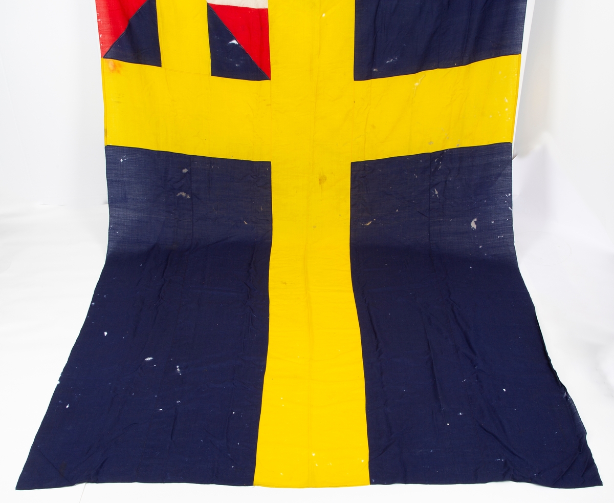 Svensk flagg med unionsmerke, "sildesalaten". Metallhempe. Møllspist og slitt.
Unionsmerket: 120 x 103

Givers datter opplyser at flagget var kjøpt på auksjon eller loppemarked på 1980 tallet. Det skal ha kommet fra båtbyggeriet på Kugrava i Son.