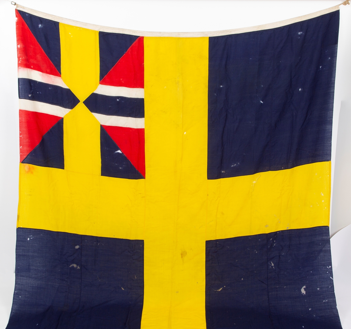 Svensk flagg med unionsmerke, "sildesalaten". Metallhempe. Møllspist og slitt.
Unionsmerket: 120 x 103

Givers datter opplyser at flagget var kjøpt på auksjon eller loppemarked på 1980 tallet. Det skal ha kommet fra båtbyggeriet på Kugrava i Son.