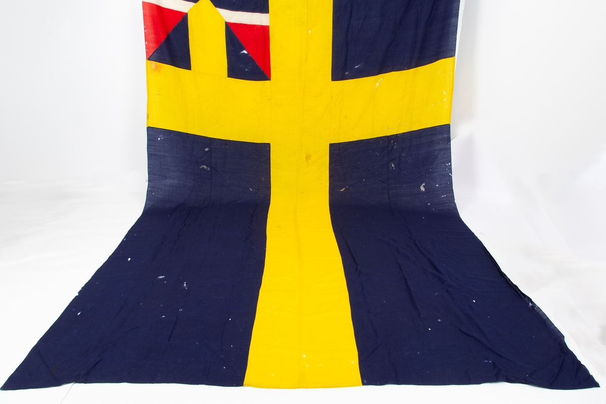 Svensk flagg med unionsmerke, "sildesalaten". Metallhempe. Møllspist og slitt.
Unionsmerket: 120 x 103

Givers datter opplyser at flagget var kjøpt på auksjon eller loppemarked på 1980 tallet. Det skal ha kommet fra båtbyggeriet på Kugrava i Son.