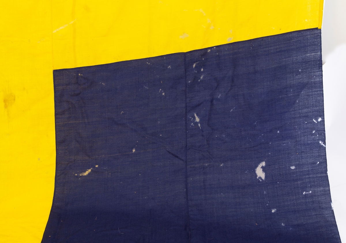 Svensk flagg med unionsmerke, "sildesalaten". Metallhempe. Møllspist og slitt.
Unionsmerket: 120 x 103

Givers datter opplyser at flagget var kjøpt på auksjon eller loppemarked på 1980 tallet. Det skal ha kommet fra båtbyggeriet på Kugrava i Son.