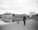 En av stadens konstaplar med myndig blick mot fotografen. Platsen är Linköpings hamn och tiden omkring 1910. Byggnaderna invid vattnet är Stångebro tvättinrättning och närmast stadens klapphus. Hamngatan i fonden kantas av hus som inte något sparats till vår tid.