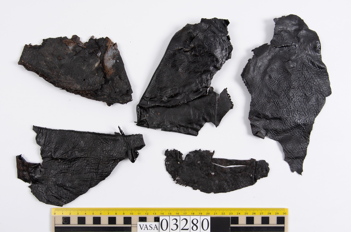 Tjugofem delar och fragment från stövel.
En sula, fyndnummer 03280. På sulans ovansida syns intryck av bindtråd. Runt ytterkanterna löper stygnshål. I hälpartiet finns hål efter träpligg.
Del av en klack, fyndnummer 03280:1, i form av fyra klacklappar samt kvarsittande träpligg.
En stropp, fyndnummer 03280:2. Ena änden är spetsformad. Andra änden är något fragmentarisk. I bägge ändar finns hål efter stygn.
Tre delar från stövelskaftet i form av tre läderstycken. Lädrstyckena är spaltade och ligger vikta. Längs sidorna löper stygnshål.
Delar och fragment av sulor, inlägg, ovanläder mm.
Merparten av lädret är spaltat och något kladdigt.