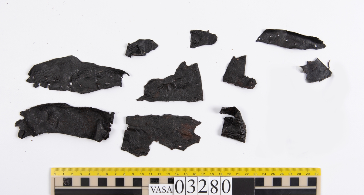 Tjugofem delar och fragment från stövel.
En sula, fyndnummer 03280. På sulans ovansida syns intryck av bindtråd. Runt ytterkanterna löper stygnshål. I hälpartiet finns hål efter träpligg.
Del av en klack, fyndnummer 03280:1, i form av fyra klacklappar samt kvarsittande träpligg.
En stropp, fyndnummer 03280:2. Ena änden är spetsformad. Andra änden är något fragmentarisk. I bägge ändar finns hål efter stygn.
Tre delar från stövelskaftet i form av tre läderstycken. Lädrstyckena är spaltade och ligger vikta. Längs sidorna löper stygnshål.
Delar och fragment av sulor, inlägg, ovanläder mm.
Merparten av lädret är spaltat och något kladdigt.