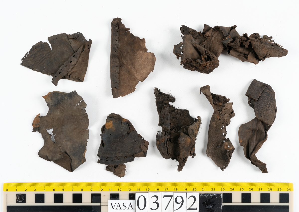 Ett 70-tal delar och fragment av stövel. Bland delarna går att urskilja en del av en klack med kvarsittande skopligg, fyra delar av ovanläder samt en stropp med avmalnande ändar. Flertalet fragment har rostfärgade utfällningar.
Lädret är tunt och sprött samt ligger hopvikt.