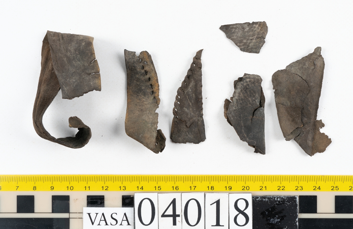 Tolv fragment av sko, varav två fragment kan vara delar från en slejf.
Lädret är mycket sprött och hårt.