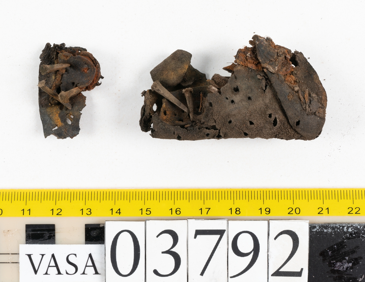 Ett 70-tal delar och fragment av stövel. Bland delarna går att urskilja en del av en klack med kvarsittande skopligg, fyra delar av ovanläder samt en stropp med avmalnande ändar. Flertalet fragment har rostfärgade utfällningar.
Lädret är tunt och sprött samt ligger hopvikt.