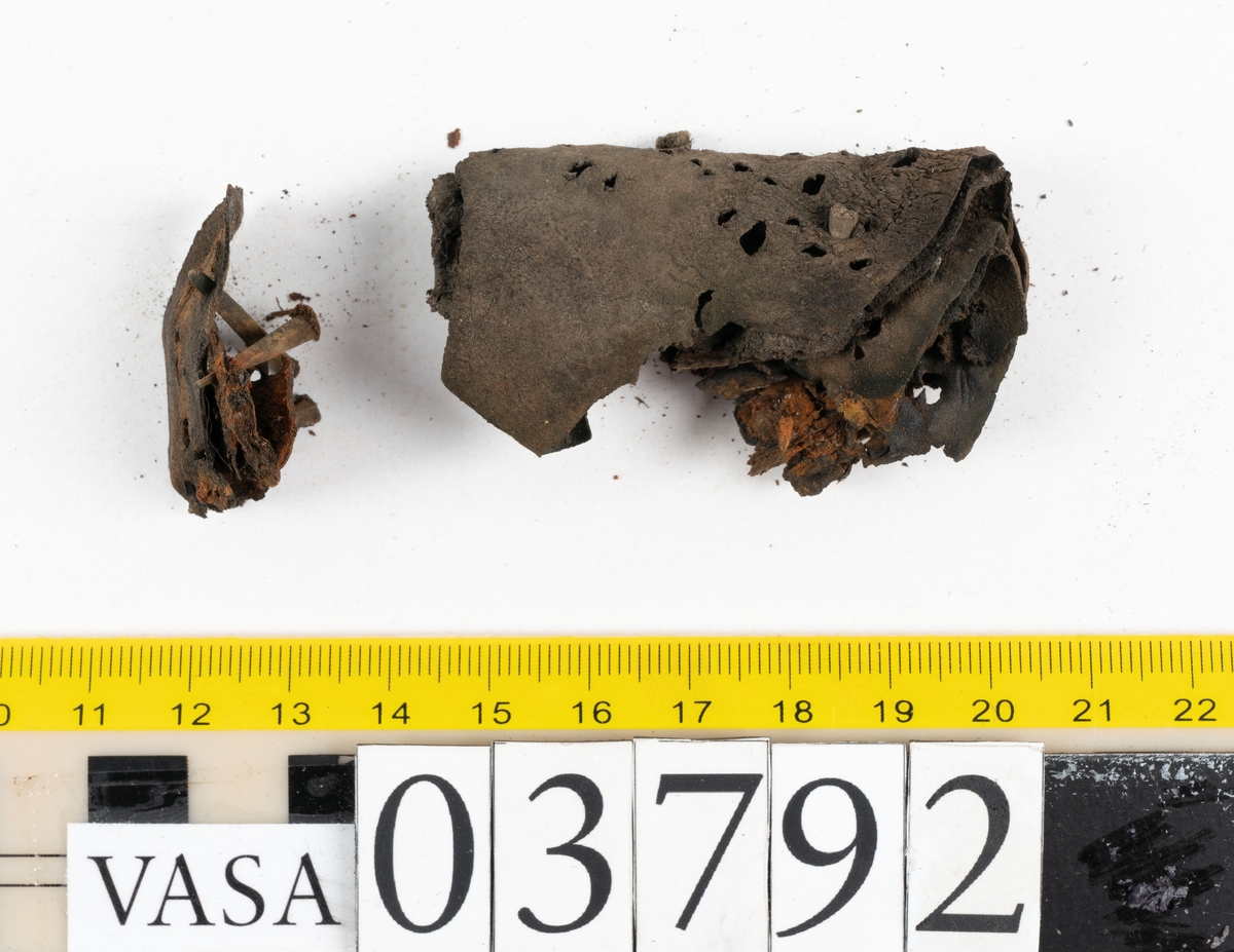 Ett 70-tal delar och fragment av stövel. Bland delarna går att urskilja en del av en klack med kvarsittande skopligg, fyra delar av ovanläder samt en stropp med avmalnande ändar. Flertalet fragment har rostfärgade utfällningar.
Lädret är tunt och sprött samt ligger hopvikt.