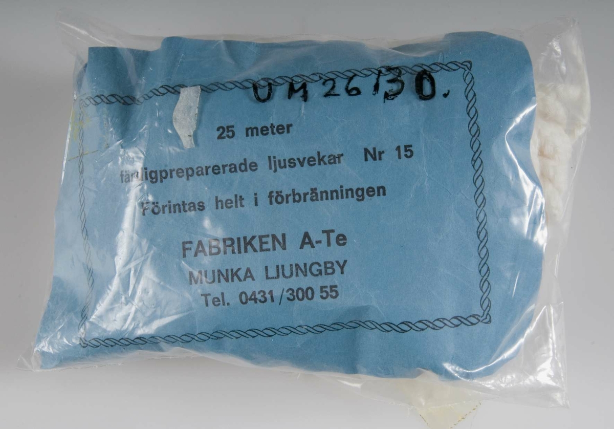 En förpackning av ofärgad mjukplast med vitt ljusvekegarn av bomull. Blå papperslapp med svart tryck: 25 meter. Färdigpreparerade ljusvekar. Nr 15. Förintas helt i förbränningen. FABRIKEN A-Te MUNKA LJUNGBY. Tel. 0431/300 55.Ljusvekegarnet har funnits till försäljning i Nolmyra handel, Nolmyra, Björklinge sn. Givarna, Eva och Tage Löjdström innehade Nolmyra handel från 1981 till 1984 då den lades ned. "Det lönade sig inte." Det var för liten kundkrets. Alla skaffade sig bil och for till stan och till Harbo och handlade. Det var besvärligt med mjölken och samarbetet med Arla. De fick ta från Gävle och betala extra. Många kunder kom ofta in och pratade. Gubben Hofvander kom varje dag. Det var roligt att ha lanthandel. Före dem hade deras son Torbjörn Löjdström handeln en tid, och de hjälpte honom. Affären låg intill Nolmyra garveri. Huset byggdes i slutet av 1800-talet och var från början handelsbod. Den gamla inredningen var kvar, men är nu borta. Innehavare innan Löjdströms var Olle Ekström, som drev den sedan 1960-talet och bodde i närheten som pensionär. Eva och Tage Löjdström bodde i Nolmyra när de  innehade handeln. De kommer från Piteå, där de tidigare haft kafé och tobaksaffär. När de flyttade till Uppsala arbetade de på Hotell Gillet.Gåva den 22 april 1994 från Eva och Tage Löjdström, Väderkvarnsgatan 21 A, Uppsala,tel: 12 93 28