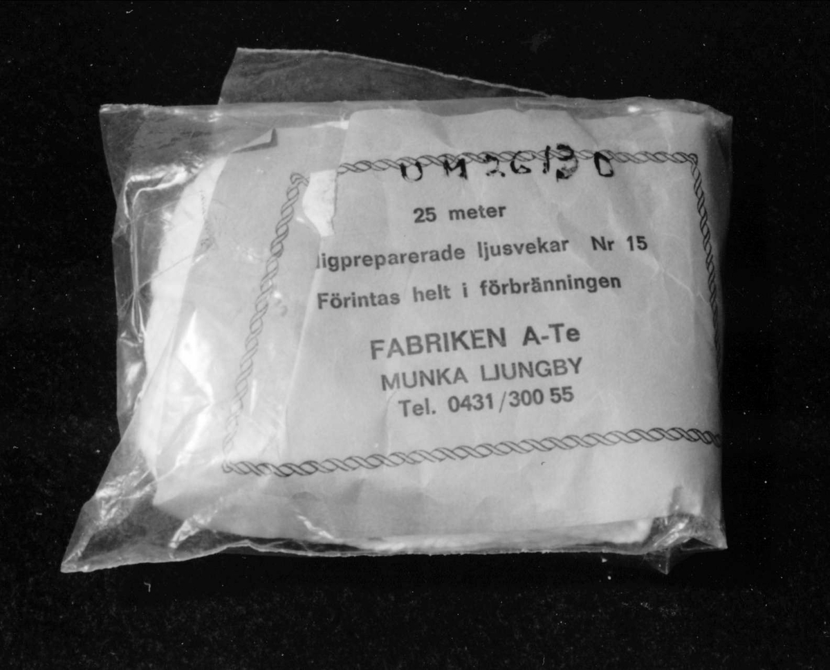 En förpackning av ofärgad mjukplast med vitt ljusvekegarn av bomull. Blå papperslapp med svart tryck: 25 meter. Färdigpreparerade ljusvekar. Nr 15. Förintas helt i förbränningen. FABRIKEN A-Te MUNKA LJUNGBY. Tel. 0431/300 55.Ljusvekegarnet har funnits till försäljning i Nolmyra handel, Nolmyra, Björklinge sn. Givarna, Eva och Tage Löjdström innehade Nolmyra handel från 1981 till 1984 då den lades ned. "Det lönade sig inte." Det var för liten kundkrets. Alla skaffade sig bil och for till stan och till Harbo och handlade. Det var besvärligt med mjölken och samarbetet med Arla. De fick ta från Gävle och betala extra. Många kunder kom ofta in och pratade. Gubben Hofvander kom varje dag. Det var roligt att ha lanthandel. Före dem hade deras son Torbjörn Löjdström handeln en tid, och de hjälpte honom. Affären låg intill Nolmyra garveri. Huset byggdes i slutet av 1800-talet och var från början handelsbod. Den gamla inredningen var kvar, men är nu borta. Innehavare innan Löjdströms var Olle Ekström, som drev den sedan 1960-talet och bodde i närheten som pensionär. Eva och Tage Löjdström bodde i Nolmyra när de  innehade handeln. De kommer från Piteå, där de tidigare haft kafé och tobaksaffär. När de flyttade till Uppsala arbetade de på Hotell Gillet.Gåva den 22 april 1994 från Eva och Tage Löjdström, Väderkvarnsgatan 21 A, Uppsala,tel: 12 93 28