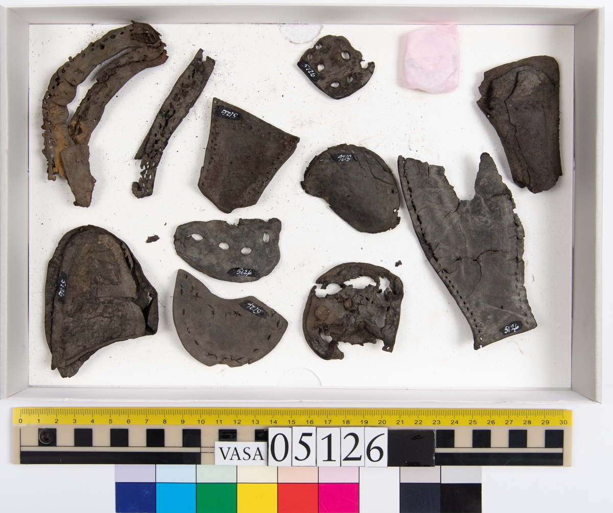 Elva delar och fragment av skobotten: sulor, inlägg, klacklapp med kvarsittande skopligg mm. Samtliga fragment har hål efter skopligg och stygn.