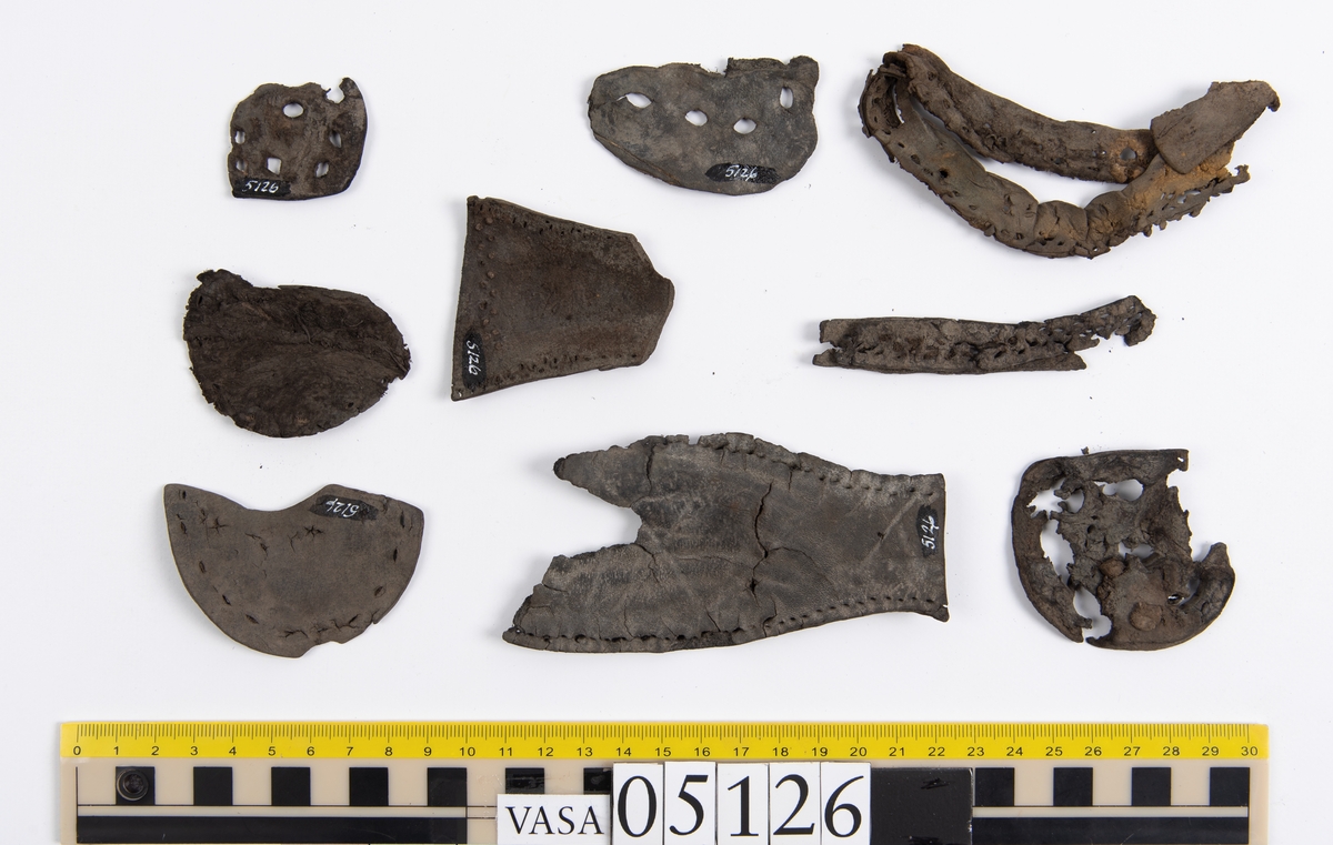 Elva delar och fragment av skobotten: sulor, inlägg, klacklapp med kvarsittande skopligg mm. Samtliga fragment har hål efter skopligg och stygn.