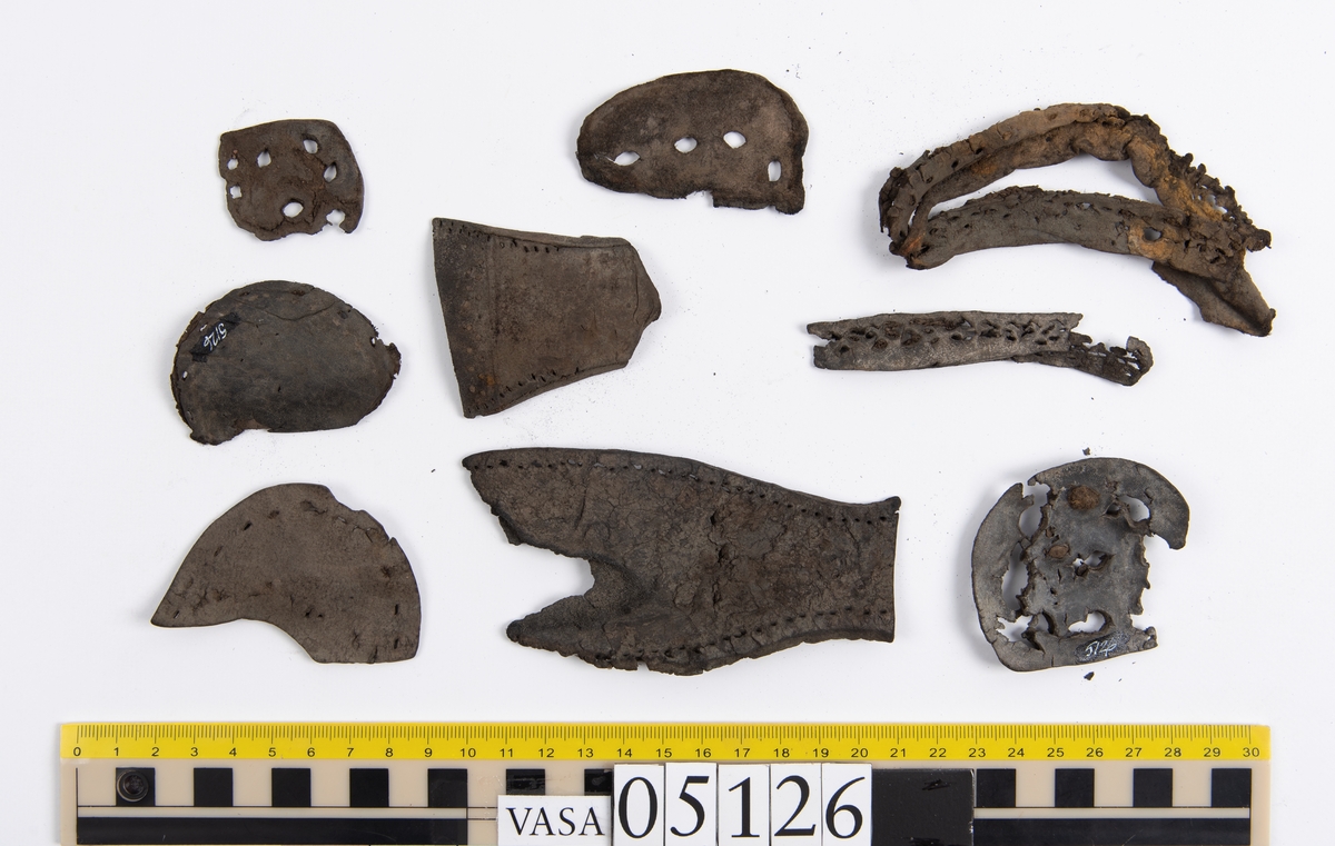 Elva delar och fragment av skobotten: sulor, inlägg, klacklapp med kvarsittande skopligg mm. Samtliga fragment har hål efter skopligg och stygn.