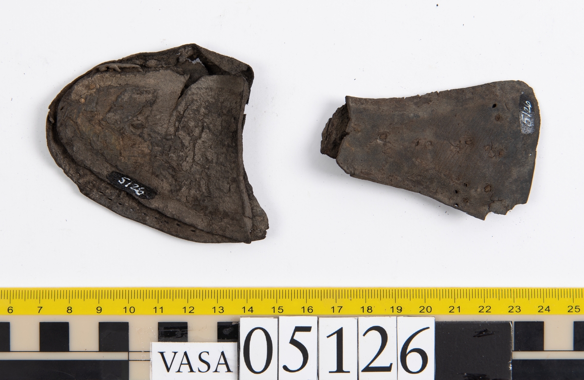 Elva delar och fragment av skobotten: sulor, inlägg, klacklapp med kvarsittande skopligg mm. Samtliga fragment har hål efter skopligg och stygn.