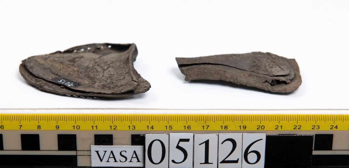 Elva delar och fragment av skobotten: sulor, inlägg, klacklapp med kvarsittande skopligg mm. Samtliga fragment har hål efter skopligg och stygn.