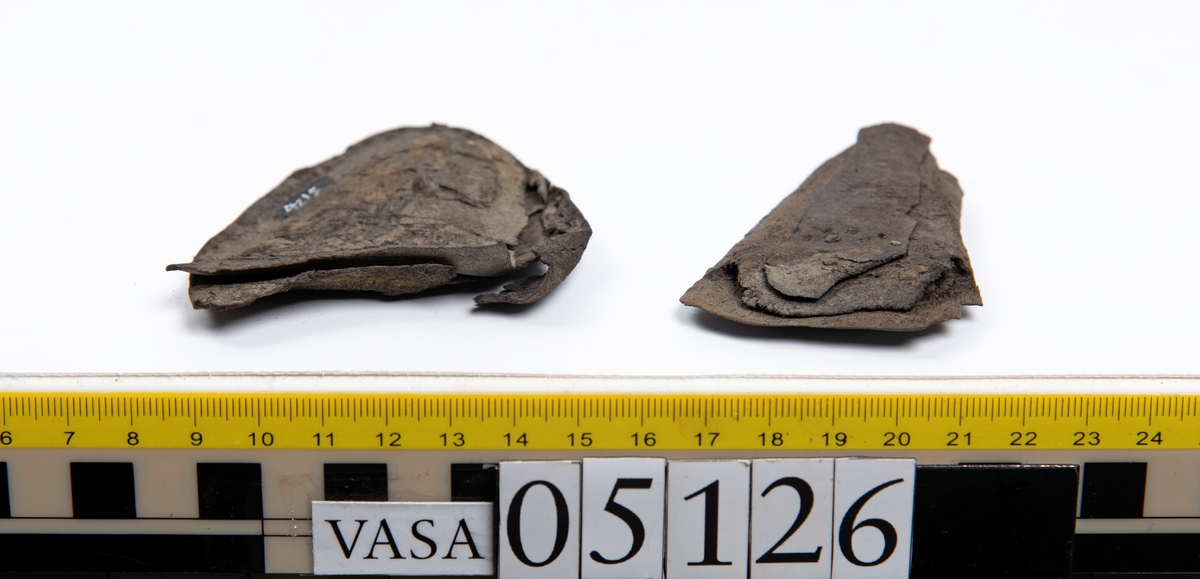 Elva delar och fragment av skobotten: sulor, inlägg, klacklapp med kvarsittande skopligg mm. Samtliga fragment har hål efter skopligg och stygn.
