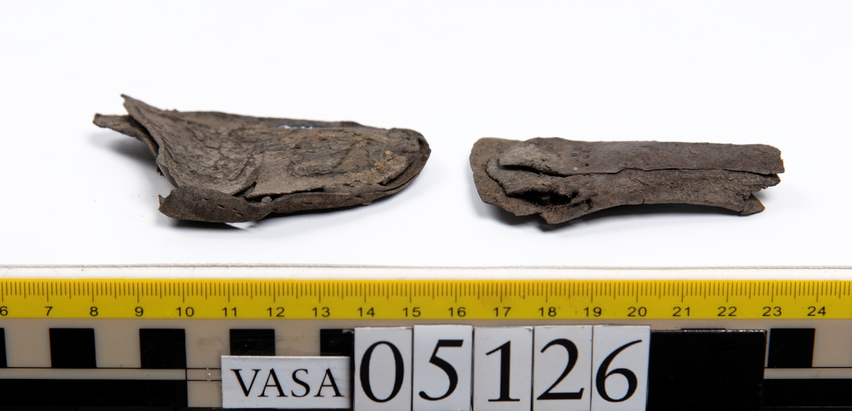 Elva delar och fragment av skobotten: sulor, inlägg, klacklapp med kvarsittande skopligg mm. Samtliga fragment har hål efter skopligg och stygn.