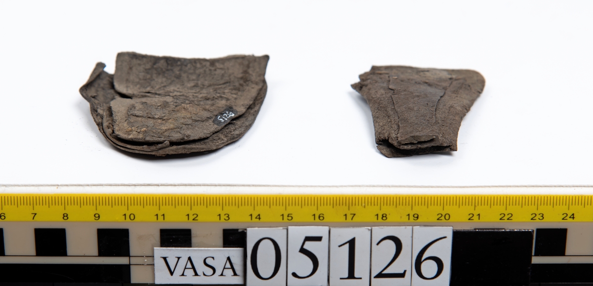 Elva delar och fragment av skobotten: sulor, inlägg, klacklapp med kvarsittande skopligg mm. Samtliga fragment har hål efter skopligg och stygn.