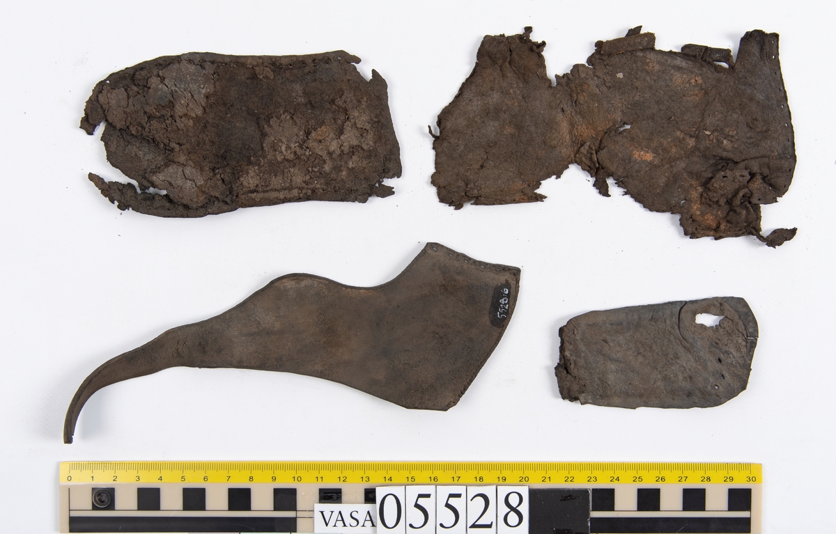 Dokumentation 1997:
Ett tjugotal delar och fragment från ett par skor.
Del av en skobotten, fyndnummer 05528. Skobottnen består av två sulor mellan vilka klacklappar sitter fästade. Sulorna och klacklapparna har monterats samman med tråd av konserveringsenheten.
En klack, fyndnummer 05528:1. Klacken är uppbyggd av sju klacklappar. Klacken har monterats samman med tråd av konserveringsenheten.
Två sulor, fyndnummer 05528:2 samt 05528:3. Sula fyndnummer 05528:3 har ett nedslitet hälparti. Sulorna och klacken är delar från den andra skobottnen som bildar par med skobotten fyndnummer 05528.
Två sulor, fyndnummer 05528:4 och 05528:5. Sulorna hör samman med någon av de två ovan nämnda skobottnarna.
Ett sidosycke med slejf, fyndnummer 05528:6. Längs med sidostyckets nedre kant löper stygnshål.
Ett 15-tal delar och fragment av holtrand, sulor mm.
Lädret är kraftigt och välbevarat.

Dokumentation 2022:
Fragment från ovanläder och ett par skobottnar (05528:4). Framstycke och sulor till öppna randskor. Tillverkade i läder. Skapades på en rak läst och bars på höger fot. Det finns regelbundna skurna dekorationer på framstycket. Klacken är reparerad med en läderlapp under sulan. Det finns tecken på delaminering på framstycket. Det finns hål i skobottens sidor och i mittensulan. Det finns inga tecken på lagningar.
För mer information, se Uppritning under Länkade filer.

Text in english:
These are one vamp fragment and a pair of bottom units (05528:4) of open side latchet shoes, made of leather, of randed construction with a patch heel, made on a straight last and worn on the right foot, with decorative pinked features across the vamp. The vamps are delaminated, and the bottom unit presents holes on both lateral sides and on the midsole. There are no signs of repairs.
For more information, go to Länkade filer: Uppritning