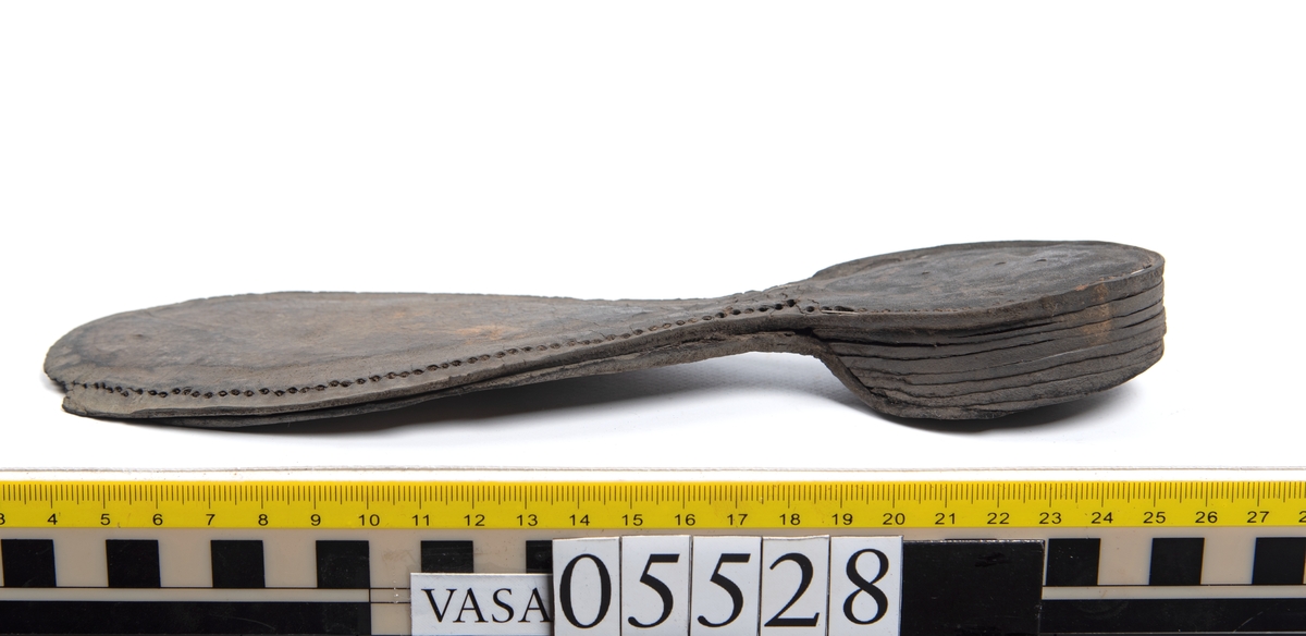 Dokumentation 1997:
Ett tjugotal delar och fragment från ett par skor.
Del av en skobotten, fyndnummer 05528. Skobottnen består av två sulor mellan vilka klacklappar sitter fästade. Sulorna och klacklapparna har monterats samman med tråd av konserveringsenheten.
En klack, fyndnummer 05528:1. Klacken är uppbyggd av sju klacklappar. Klacken har monterats samman med tråd av konserveringsenheten.
Två sulor, fyndnummer 05528:2 samt 05528:3. Sula fyndnummer 05528:3 har ett nedslitet hälparti. Sulorna och klacken är delar från den andra skobottnen som bildar par med skobotten fyndnummer 05528.
Två sulor, fyndnummer 05528:4 och 05528:5. Sulorna hör samman med någon av de två ovan nämnda skobottnarna.
Ett sidosycke med slejf, fyndnummer 05528:6. Längs med sidostyckets nedre kant löper stygnshål.
Ett 15-tal delar och fragment av holtrand, sulor mm.
Lädret är kraftigt och välbevarat.

Dokumentation 2022:
Fragment från ovanläder och ett par skobottnar (05528:4). Framstycke och sulor till öppna randskor. Tillverkade i läder. Skapades på en rak läst och bars på höger fot. Det finns regelbundna skurna dekorationer på framstycket. Klacken är reparerad med en läderlapp under sulan. Det finns tecken på delaminering på framstycket. Det finns hål i skobottens sidor och i mittensulan. Det finns inga tecken på lagningar.
För mer information, se Uppritning under Länkade filer.

Text in english:
These are one vamp fragment and a pair of bottom units (05528:4) of open side latchet shoes, made of leather, of randed construction with a patch heel, made on a straight last and worn on the right foot, with decorative pinked features across the vamp. The vamps are delaminated, and the bottom unit presents holes on both lateral sides and on the midsole. There are no signs of repairs.
For more information, go to Länkade filer: Uppritning