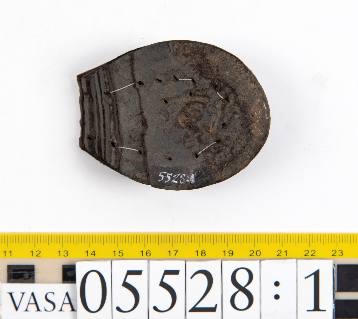 Dokumentation 1997:
Ett tjugotal delar och fragment från ett par skor.
Del av en skobotten, fyndnummer 05528. Skobottnen består av två sulor mellan vilka klacklappar sitter fästade. Sulorna och klacklapparna har monterats samman med tråd av konserveringsenheten.
En klack, fyndnummer 05528:1. Klacken är uppbyggd av sju klacklappar. Klacken har monterats samman med tråd av konserveringsenheten.
Två sulor, fyndnummer 05528:2 samt 05528:3. Sula fyndnummer 05528:3 har ett nedslitet hälparti. Sulorna och klacken är delar från den andra skobottnen som bildar par med skobotten fyndnummer 05528.
Två sulor, fyndnummer 05528:4 och 05528:5. Sulorna hör samman med någon av de två ovan nämnda skobottnarna.
Ett sidosycke med slejf, fyndnummer 05528:6. Längs med sidostyckets nedre kant löper stygnshål.
Ett 15-tal delar och fragment av holtrand, sulor mm.
Lädret är kraftigt och välbevarat.

Dokumentation 2022:
Fragment från ovanläder och ett par skobottnar (05528:4). Framstycke och sulor till öppna randskor. Tillverkade i läder. Skapades på en rak läst och bars på höger fot. Det finns regelbundna skurna dekorationer på framstycket. Klacken är reparerad med en läderlapp under sulan. Det finns tecken på delaminering på framstycket. Det finns hål i skobottens sidor och i mittensulan. Det finns inga tecken på lagningar.
För mer information, se Uppritning under Länkade filer.

Text in english:
These are one vamp fragment and a pair of bottom units (05528:4) of open side latchet shoes, made of leather, of randed construction with a patch heel, made on a straight last and worn on the right foot, with decorative pinked features across the vamp. The vamps are delaminated, and the bottom unit presents holes on both lateral sides and on the midsole. There are no signs of repairs.
For more information, go to Länkade filer: Uppritning