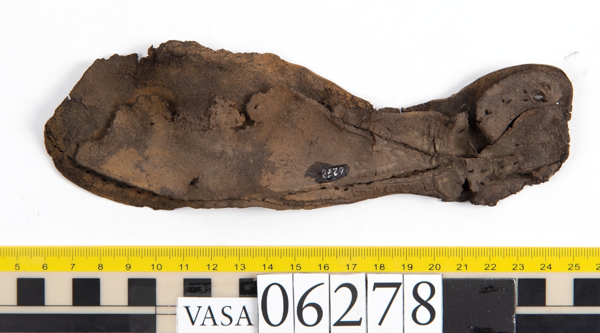 Sula, klacklapp samt större och mindre fragment från skobotten. Totalt ett 50-tal delar och fragment. Sulan är något fragmentarisk samt försedd med en ritsad linje som löper innanför ytterkanten. På klacklappen syns hål efter träpligg.
Klacklädret och sullädret är torrt och styvt medan en stor del av fragmenten består av mjukt och böjligt läder.