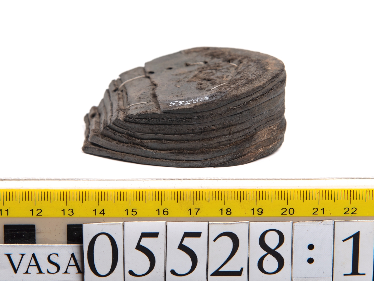 Dokumentation 1997:
Ett tjugotal delar och fragment från ett par skor.
Del av en skobotten, fyndnummer 05528. Skobottnen består av två sulor mellan vilka klacklappar sitter fästade. Sulorna och klacklapparna har monterats samman med tråd av konserveringsenheten.
En klack, fyndnummer 05528:1. Klacken är uppbyggd av sju klacklappar. Klacken har monterats samman med tråd av konserveringsenheten.
Två sulor, fyndnummer 05528:2 samt 05528:3. Sula fyndnummer 05528:3 har ett nedslitet hälparti. Sulorna och klacken är delar från den andra skobottnen som bildar par med skobotten fyndnummer 05528.
Två sulor, fyndnummer 05528:4 och 05528:5. Sulorna hör samman med någon av de två ovan nämnda skobottnarna.
Ett sidosycke med slejf, fyndnummer 05528:6. Längs med sidostyckets nedre kant löper stygnshål.
Ett 15-tal delar och fragment av holtrand, sulor mm.
Lädret är kraftigt och välbevarat.

Dokumentation 2022:
Fragment från ovanläder och ett par skobottnar (05528:4). Framstycke och sulor till öppna randskor. Tillverkade i läder. Skapades på en rak läst och bars på höger fot. Det finns regelbundna skurna dekorationer på framstycket. Klacken är reparerad med en läderlapp under sulan. Det finns tecken på delaminering på framstycket. Det finns hål i skobottens sidor och i mittensulan. Det finns inga tecken på lagningar.
För mer information, se Uppritning under Länkade filer.

Text in english:
These are one vamp fragment and a pair of bottom units (05528:4) of open side latchet shoes, made of leather, of randed construction with a patch heel, made on a straight last and worn on the right foot, with decorative pinked features across the vamp. The vamps are delaminated, and the bottom unit presents holes on both lateral sides and on the midsole. There are no signs of repairs.
For more information, go to Länkade filer: Uppritning