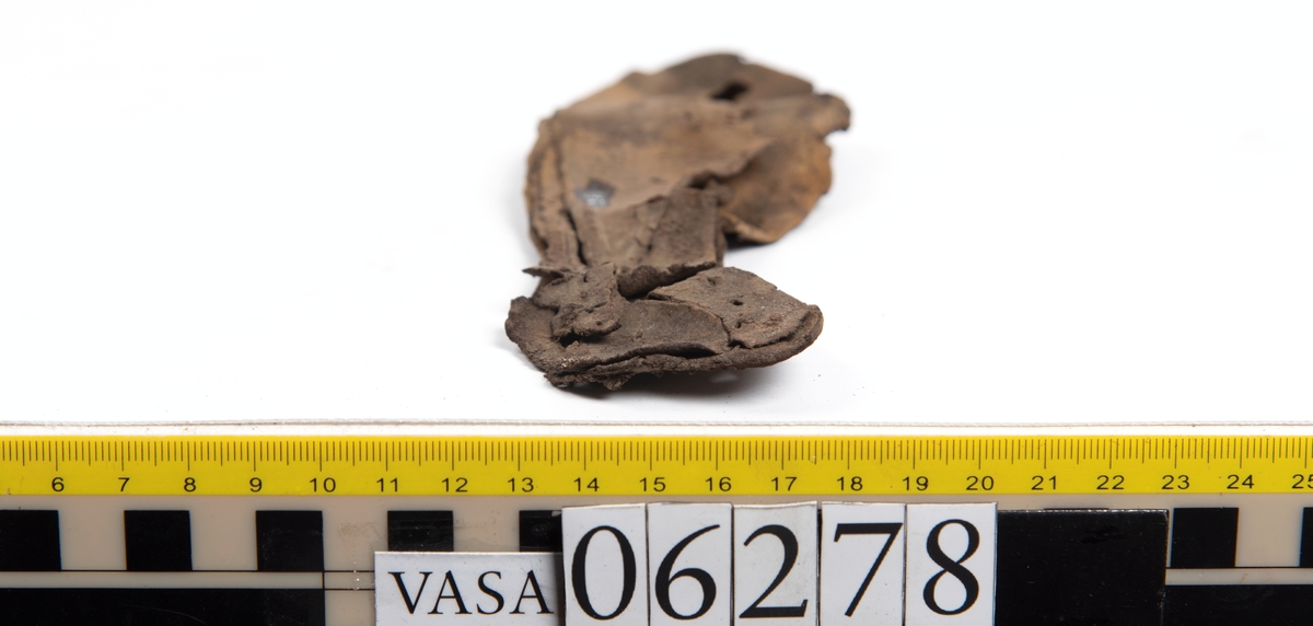 Sula, klacklapp samt större och mindre fragment från skobotten. Totalt ett 50-tal delar och fragment. Sulan är något fragmentarisk samt försedd med en ritsad linje som löper innanför ytterkanten. På klacklappen syns hål efter träpligg.
Klacklädret och sullädret är torrt och styvt medan en stor del av fragmenten består av mjukt och böjligt läder.