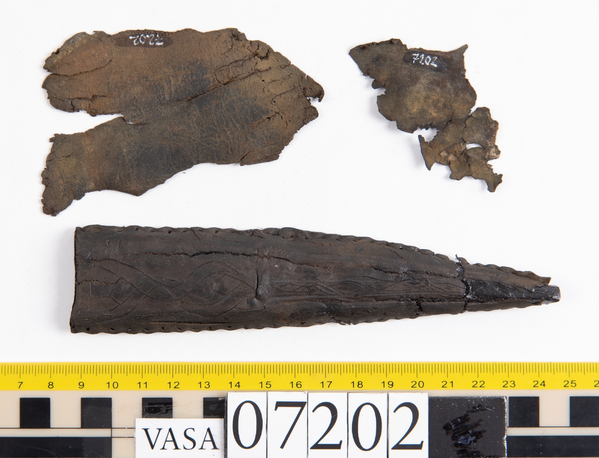 Framstycke till en knivslida. Bakstycket samt en del av slidspetsen saknas. Knivslidan är försedd med en inristad bandornamentik. Längs med sidorna löper stygnshål. Knivslidans öppning är skuren rakt. Knivslidan har monterats på svart kartong av konserveringsenheten.
Två större och sex mindre fragment med hål efter stygn. Eventuellt kan fragmenten härröra från knivslidans bakstycke. Fragmenten är spröda och fragmentariska samt har rostfärgade fläckar.