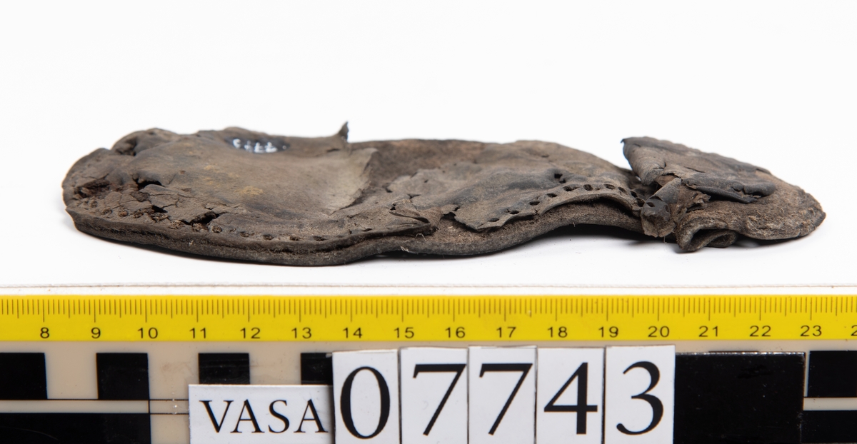 En sula. Sulan ligger vikt. Kvarsittande tråd samt hål efter skopligg. Lädret är spaltat. Två lösa mindre fragment.